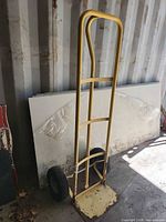 Full view of yellow metal hand truck standing upright