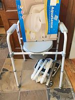 Overall view of commode with boxed toilet seat and accessories beneath