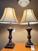 Two matching brushed bronze table lamps with beige shades displayed on table