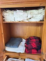Stacked white/off-white sheet sets on top shelf, blue throw, white coverlet, red/black buffalo plaid sheets on lower shelf