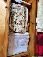 Drawer showing folded floral-print linen over white embroidered sheer panels and additional linens