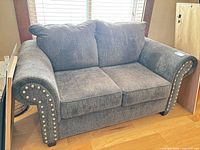 Front view of charcoal grey upholstered loveseat with nailhead trim and two seat cushions