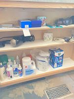Shelving showing Waterpik box, bagged irrigator, hairdryer, ceramic tumbler, assorted solution bottles