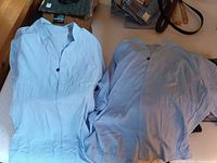 Two light blue short-sleeve shirts laid out on bed