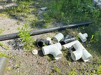 Group of PVC and ABS fittings with long black pipe on ground