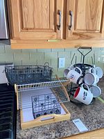 Overview of lap tray, bamboo dish rack, black metal baskets, mug tree with mugs on countertop