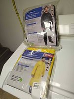 Both sealed packages of WetSkins rainwear: black motorsport rainsuit XXL and yellow raincoat XXL