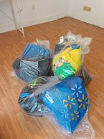 Three clear plastic bags on floor containing numerous reusable bags