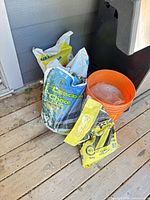 Three partial ice melt bags and orange bucket on deck