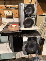 Two Sony speakers stacked, black subwoofer below, Toshiba DVD player and speaker wire on shelf