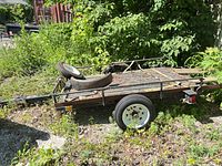Side view of utility trailer showing frame, deck, side rails, wheel and spare
