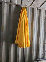 Closed yellow market umbrella against wall