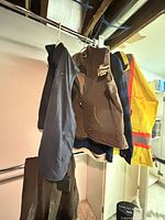Group of hanging garments: Berne vest, Ororo vest sleeve, Berne overall pants, Red Head plaid jacket partially visible