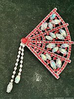 Full view of brooch showing fan shape, red stones, dangle chains