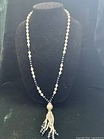 Necklace displayed full length on bust showing ivory faux pearls, black beads, tassel