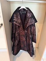 Front view of purple floral jacquard long coat hanging, shows overall design and shawl collar