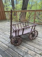 Full view of wooden farm cart on deck showing wheels, rails, and pull shaft