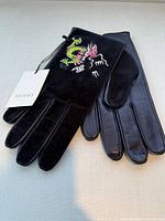 Pair of black Gucci gloves, one showing dragon embroidery, attached tag visible