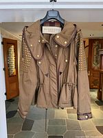Front view of jacket on hanger displaying overall style, color, and studded detailing