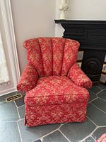 Front angle view of red floral upholstered armchair showing channel-back, arms, seat, and skirt