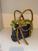 Front view black speckled foam handbag with green fabric top, mustard velvet handles, silver chain