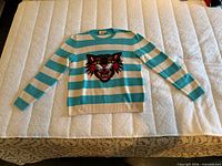 Full front view of striped Gucci sweater laid flat on bed