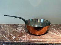 Side view of hammered copper saucepan on marble surface