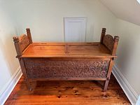 Front view of carved wood chest showing lid, carvings, legs