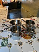 Four stainless steel pots on tiled countertop displaying interiors and handles