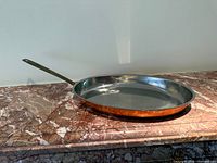 Top angled view of oval copper-clad pan on marble surface