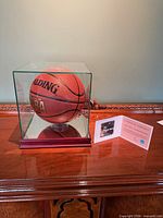 Basketball in glass display case on wooden base with COA card beside it