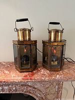 Front view of both brass lantern lamps illuminated on marble surface