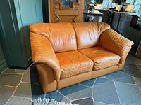 Front angled view of tan leather loveseat showing overall design and condition