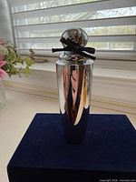 Front view of silver cylindrical So Pretty de Cartier 50 ml Eau de Toilette bottle on dark blue base