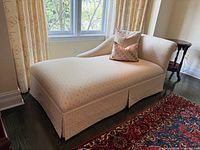 Full view of cream patterned chaise lounge with pillows against window and curtains