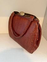 Front angled view showing crocodile leather texture, handles, and clasp