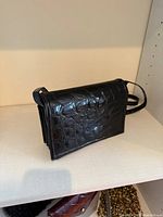 Front view of black croc-embossed leather handbag with strap