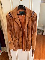 Front view of suede fringe jacket showing overall design, pockets, shoulder appliqués and concho