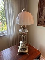Full view of lamp on table showing metal base and frosted shade