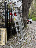Two aluminum ladders leaning against fence: extension ladder left, step ladder right