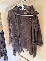 Front view of sweater on hanger showing overall style, distressing, pockets and hood
