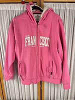 Full front view of pink Exist hoodie on hanger