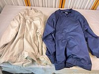 Beige and navy Nike windbreaker jackets side by side on table