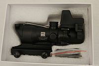 Scope seated in white foam box with mount and accessory bag visible