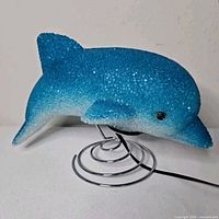 Left side view of blue popcorn plastic dolphin lamp on chrome spiral base with power cord visible