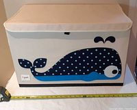 Front view of canvas storage bin showing whale applique and tape measure for width