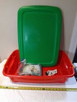 Red tub with green lid/baseplate shown upright, bag of bricks inside
