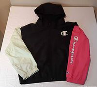 Front of color-block Champion windbreaker showing hood, zipper, cream left sleeve, pink right sleeve, logos