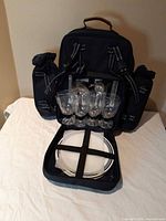 Backpack opened showing plates, glasses, cutlery, and bottle holders