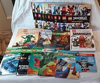 All twelve LEGO Ninjago books laid out – two hardcovers at front left, nine Papercutz graphic novels in two rows, Zane’s manual bottom row